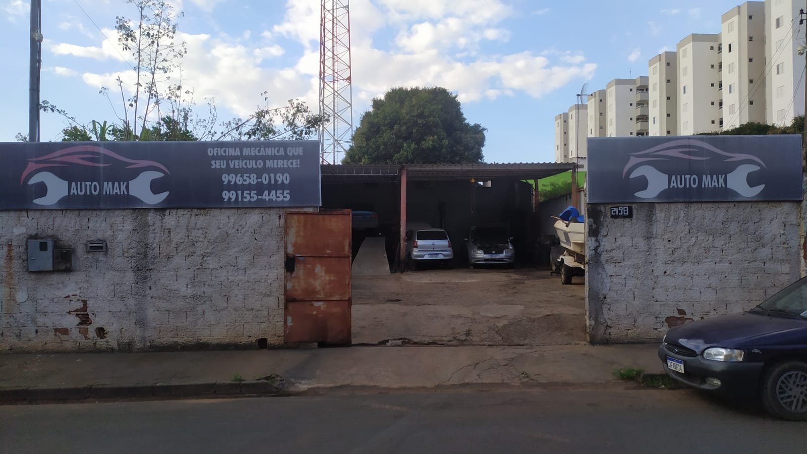 Fachada da oficina mecânica Auto Mak com um muro, banners em cima e um portão grande aberto no meio